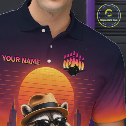 A close-up of a person wearing a dark navy polo shirt with a colorful retro-style graphic print. The design features a large orange sunset, a raccoon in a hat and sunglasses, bowling pins, a bowling ball, and the text 'YOUR NAME' on the chest.