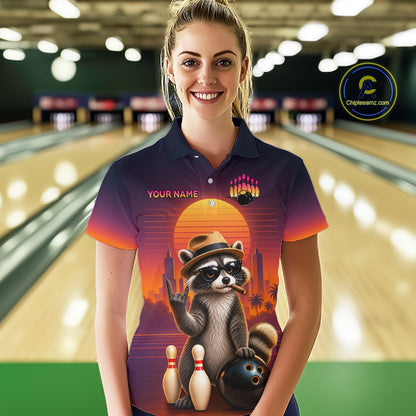 A woman wearing a custom bowling-themed short-sleeve polo shirt with a raccoon graphic, bowling pins, and a sunset design, set against a blurred bowling alley background.