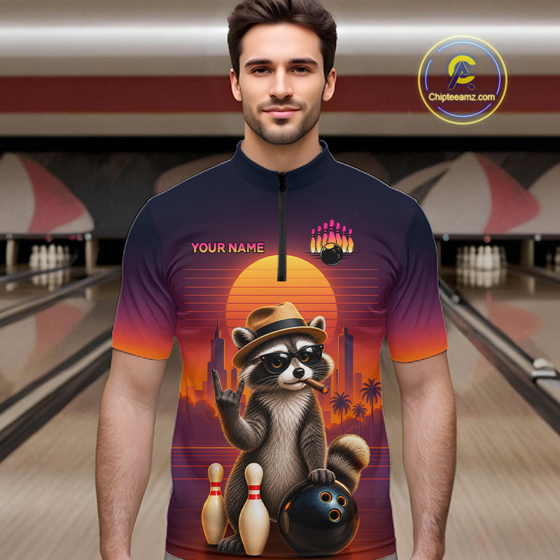 A man wearing a short-sleeve quarter-zip bowling-themed graphic shirt with a raccoon illustration and sunset gradient, standing in a bowling alley. The shirt includes 'YOUR NAME' text and a bowling pins graphic.