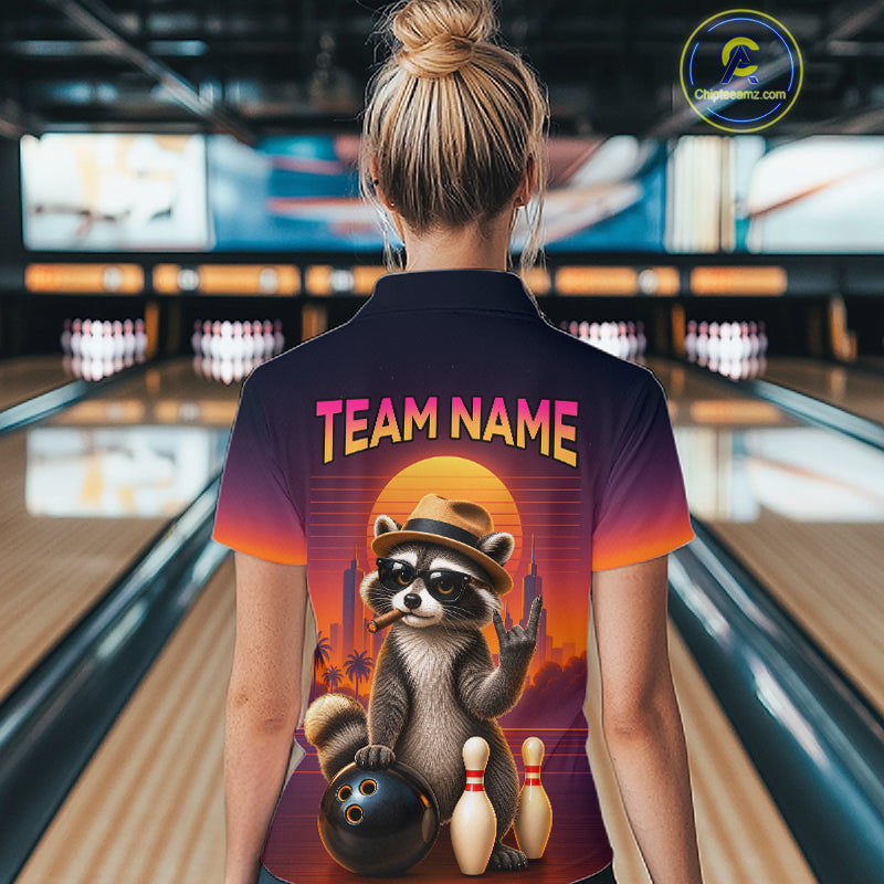 A woman viewed from behind wearing a bowling-themed short-sleeve polo shirt with a colorful raccoon graphic and the text 'TEAM NAME' on the back, standing in a bowling alley.