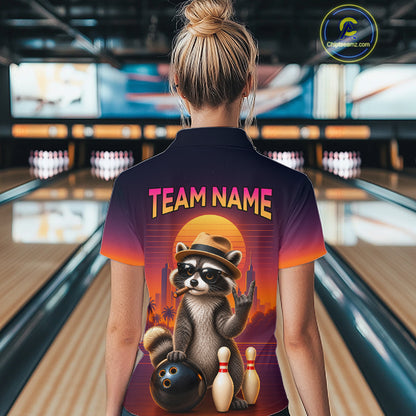 A woman viewed from behind wearing a bowling-themed short-sleeve polo shirt with a colorful raccoon graphic and the text 'TEAM NAME' on the back, standing in a bowling alley.