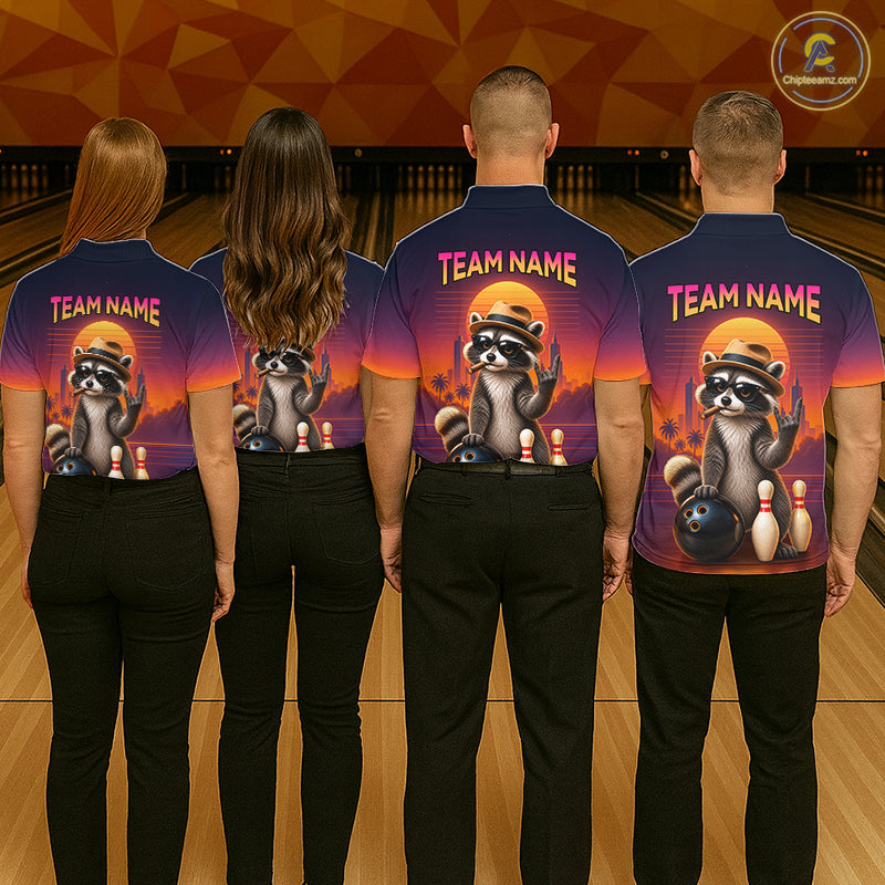 Four people standing with their backs to the camera in a bowling alley, wearing matching dark blue short-sleeve shirts with a large raccoon graphic and the text 'TEAM NAME' on the back. The shirts have a purple-to-orange gradient design with bowling-themed artwork.