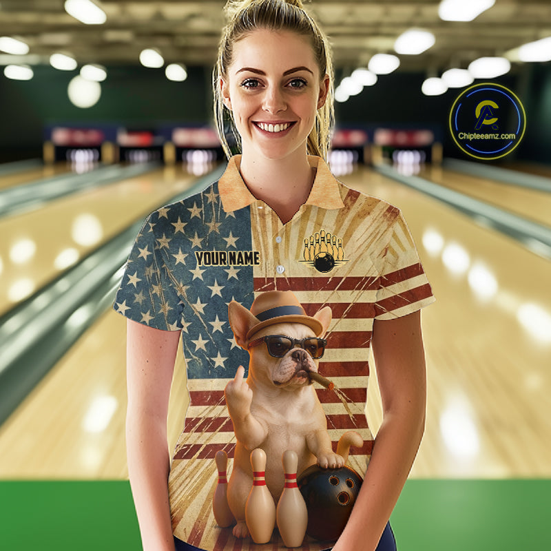 A woman stands in a bowling alley wearing a custom-printed polo shirt. The shirt features a split design: one side has an American flag pattern with the text 'YOUR NAME' and 'BOWLING CLUB', while the other side shows a small dog wearing a hat and sunglasses with bowling pins and a bowling ball.