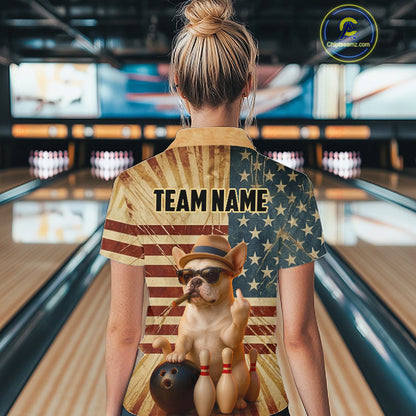 A woman viewed from behind in a bowling alley wearing a short-sleeve button-up shirt with a patriotic American flag design and a cartoon dog graphic. The shirt has 'TEAM NAME' printed across the back.