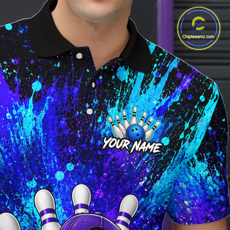 A close-up of a person wearing a short-sleeve polo shirt with a black collar and a vivid blue, purple, and black paint-splatter graphic. The shirt features a bowling-themed chest design with a blue bowling ball, white pins, and the text 'YOUR NAME'.