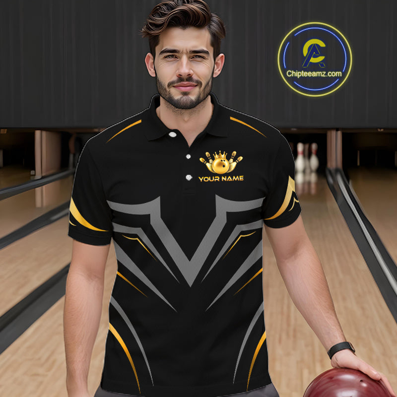 A man wearing a black bowling polo shirt with gray and gold graphic patterns and a gold crown logo on the chest, standing in a bowling alley holding a bowling ball. 