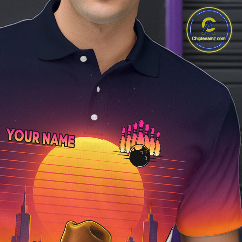 A close-up of a person wearing a dark navy polo shirt with a colorful retro bowling graphic on the front. The design features a large yellow-orange sun, pink bowling pins, a black bowling ball, and the text 'YOUR NAME' in pink.