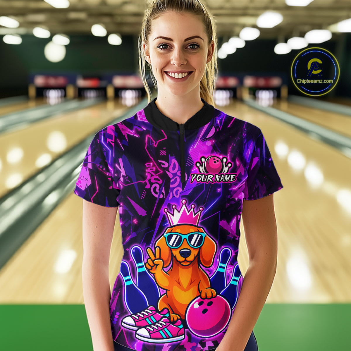 Woman wearing a black and purple bowling quarter zip shirt featuring a cartoon dachshund wearing sunglasses and a crown, holding a pink bowling ball, with custom your name text.