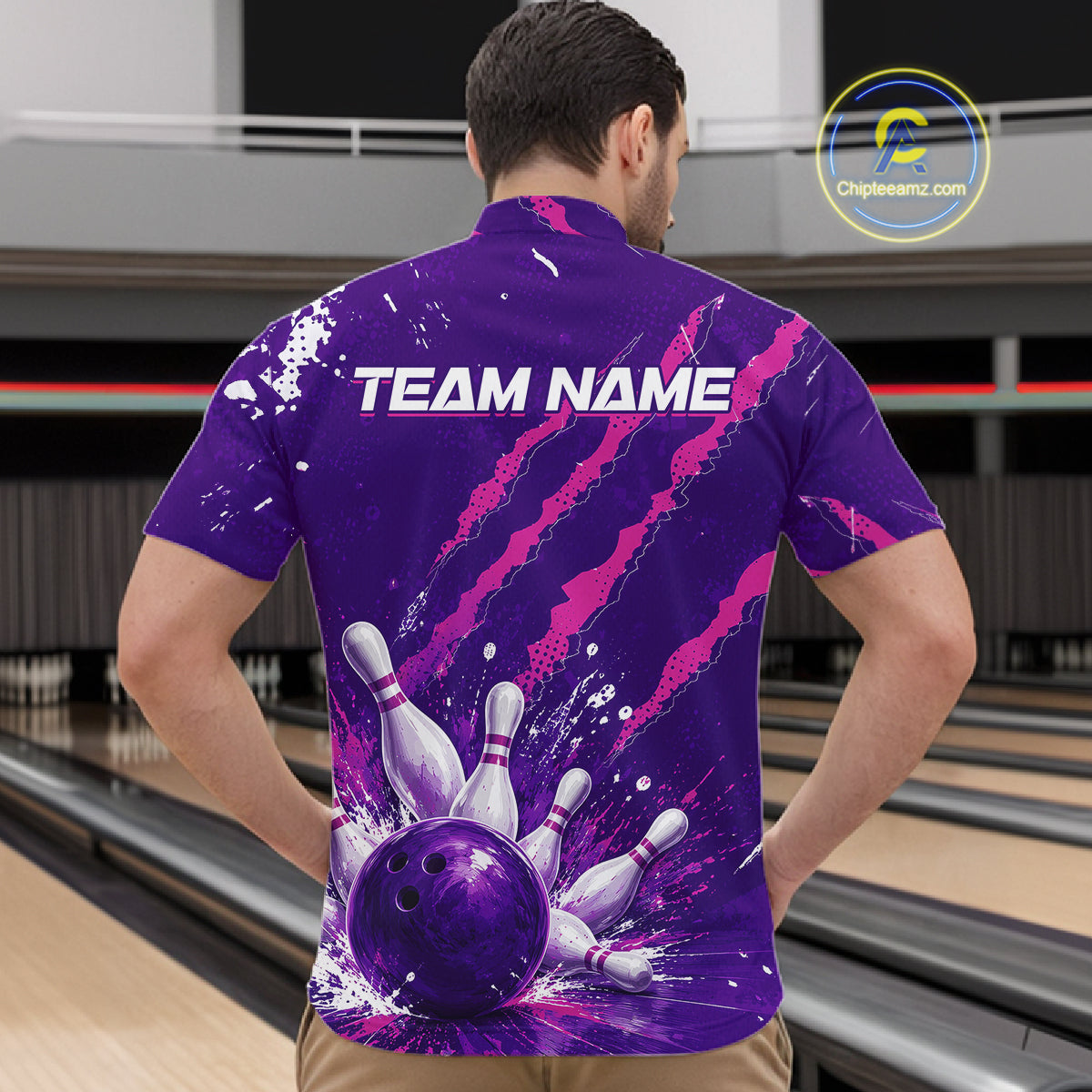 A man viewed from behind wearing a purple bowling-themed short-sleeve button-up shirt with a large bowling pin and ball graphic on the back, plus the text 'TEAM NAME'. The background shows bowling lanes in a real indoor bowling alley.