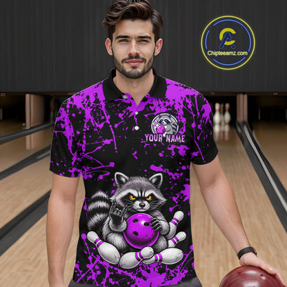 A man wearing a black and purple bowling-themed polo shirt with a raccoon graphic holding a bowling ball, standing in a bowling alley. 