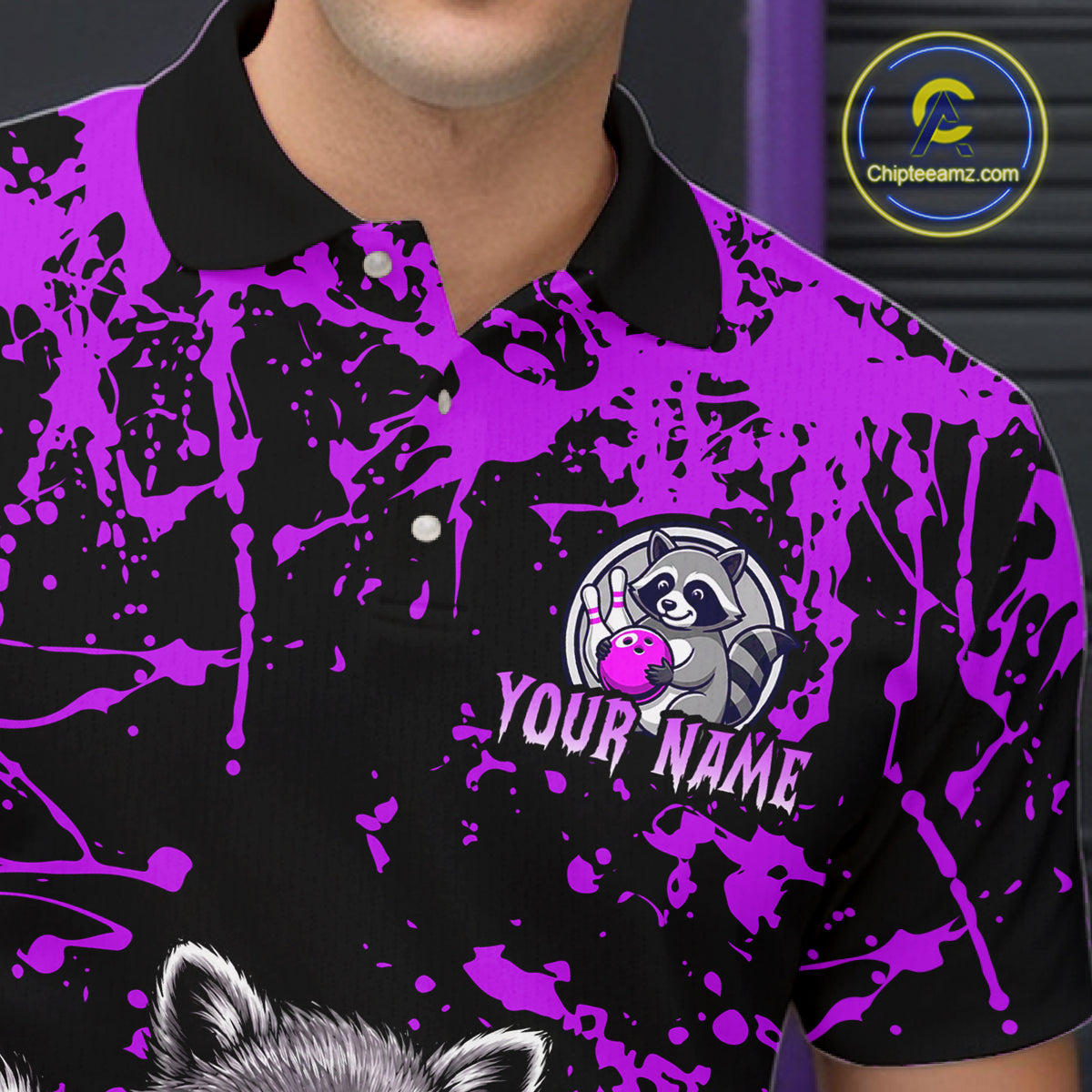 A close-up of a man wearing a black and bright purple polo shirt with a splatter print, a custom raccoon logo, and the text 'YOUR NAME'.