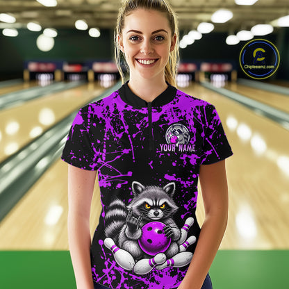 A woman standing in a bowling alley wearing a custom short-sleeve bowling t-shirt with a black and purple splatter design, featuring a raccoon holding a bowling ball and pins on the front, and a customizable name patch on the chest.