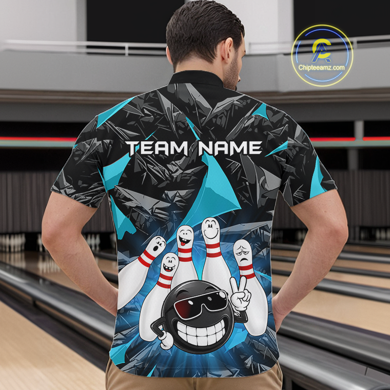 A man standing in a bowling alley wearing a custom bowling-themed short-sleeve collared shirt, viewed from behind. The shirt features a black and gray geometric pattern with bright blue accents, cartoon bowling pins, a cartoon bowling ball with sunglasses, and the text 'TEAM NAME'.