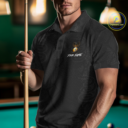 A man in a dark gray patterned polo shirt holding a pool cue in a pool hall setting. The shirt features a custom bunny graphic with a gold eye and the text 'YOUR NAME' on the left chest.