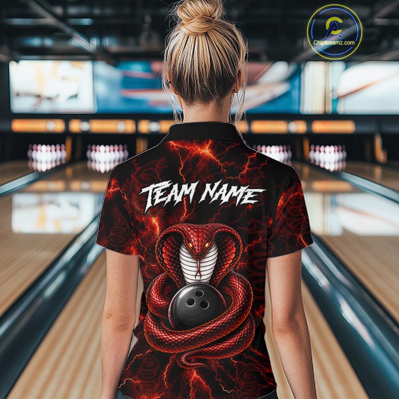 A woman viewed from behind wearing a black short-sleeve bowling shirt with a red lightning and snake graphic, standing in a bowling alley. The shirt features the text 'TEAM NAME' and a large red snake coiled around a bowling ball.