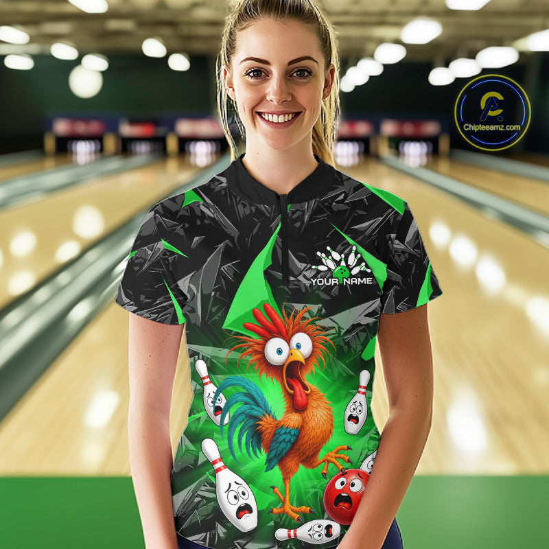 A woman stands in a bowling alley wearing a short-sleeve bowling shirt with a black and green geometric pattern and a large cartoon rooster graphic on the front. The shirt has a white 'YOUR NAME' placeholder logo on the chest.