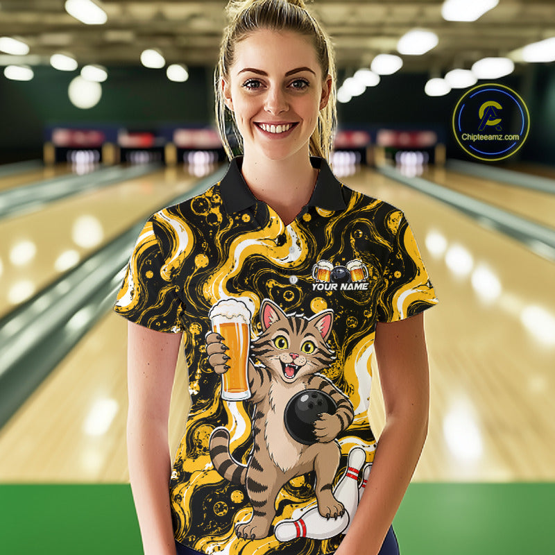 A woman stands in a bowling alley wearing a short-sleeve polo shirt with a bold black and yellow abstract pattern and a large graphic of a cartoon cat holding a bowling ball and beer glass. The shirt also has a 'YOUR NAME' customization area on the chest.