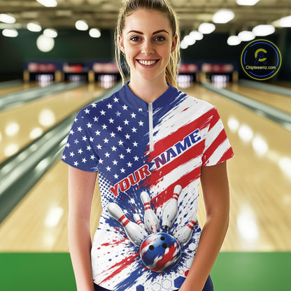 A woman stands in a bowling alley wearing a short-sleeve zip-front bowling jersey with a red, white, and blue American flag design, bowling pins, and a bowling ball graphic. The jersey has placeholder text 'YOUR NAME'.