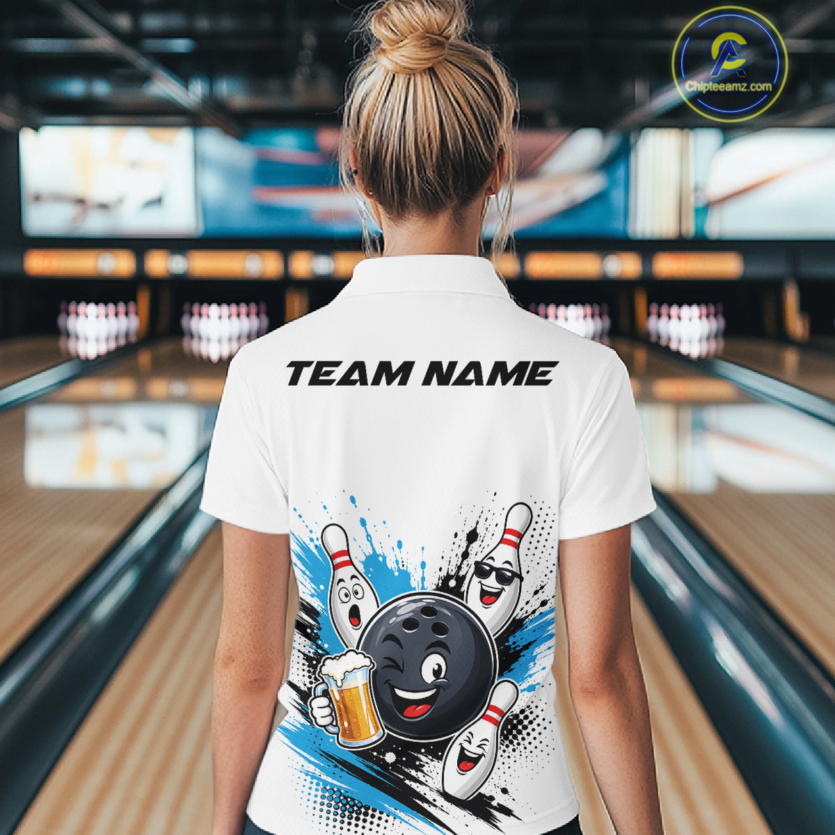 A woman viewed from behind wearing a white bowling-themed short-sleeve polo shirt with a large cartoon bowling ball and pins graphic on the back, standing in a bowling alley.