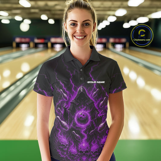 A woman wearing a black short-sleeve polo shirt with a purple and black grim reaper bowling graphic and the text 'YOUR NAME' on the chest, standing in a bowling alley. 