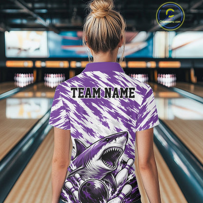 Person wearing a purple and white bowling shirt with a shark design and 'TEAM NAME' text in a bowling alley.