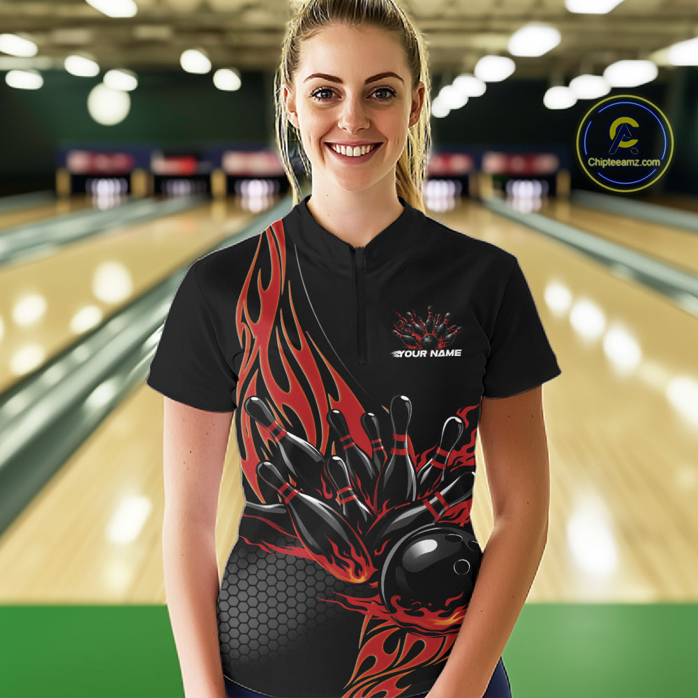 Female model front view inside bowling center wearing black quarter zip shirt featuring red flame bowling ball knocking down pins artwork