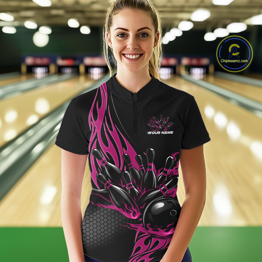 Female model front view in bowling alley wearing black quarter zip shirt featuring pink flame bowling ball hitting pins illustration