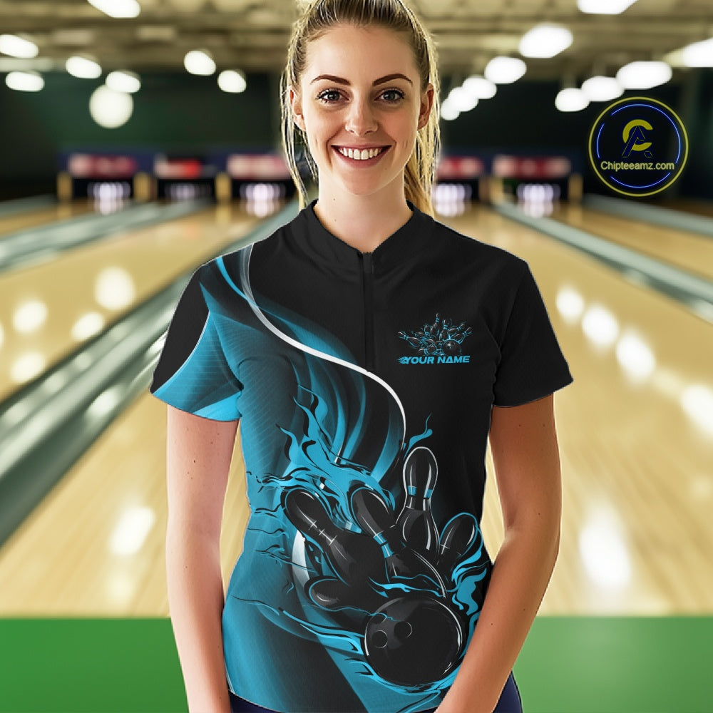 Female model front view in bowling center wearing black and blue quarter zip shirt showcasing flame bowling action graphic design