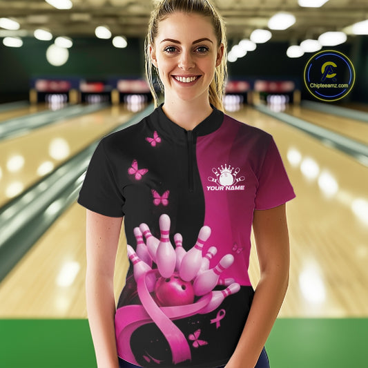 Front view of a female model in a black and pink bowling quarter zip featuring pink ribbon artwork, small butterflies, and bowling-themed accents at the bowling lane.