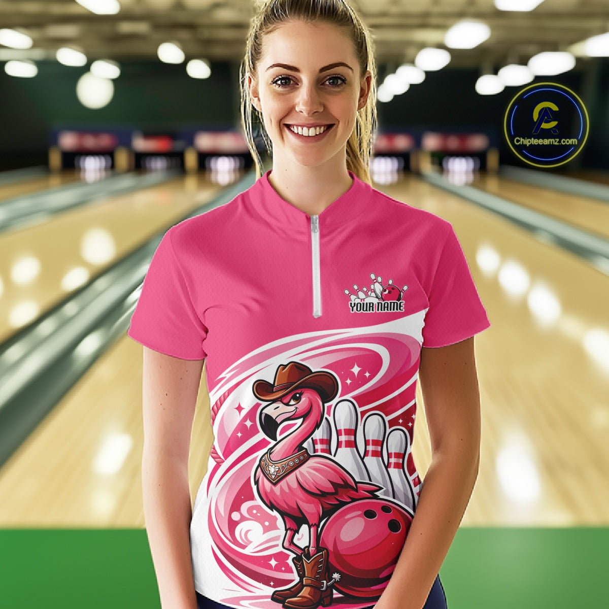 Female model wearing a pink bowling quarter-zip shirt at a bowling lane with a cowboy flamingo and bowling ball artwork.