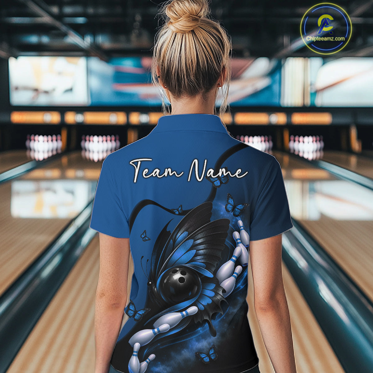 Back view of a female model at a bowling lane wearing a blue and black bowling quarter-zip shirt featuring a butterfly around a bowling ball.