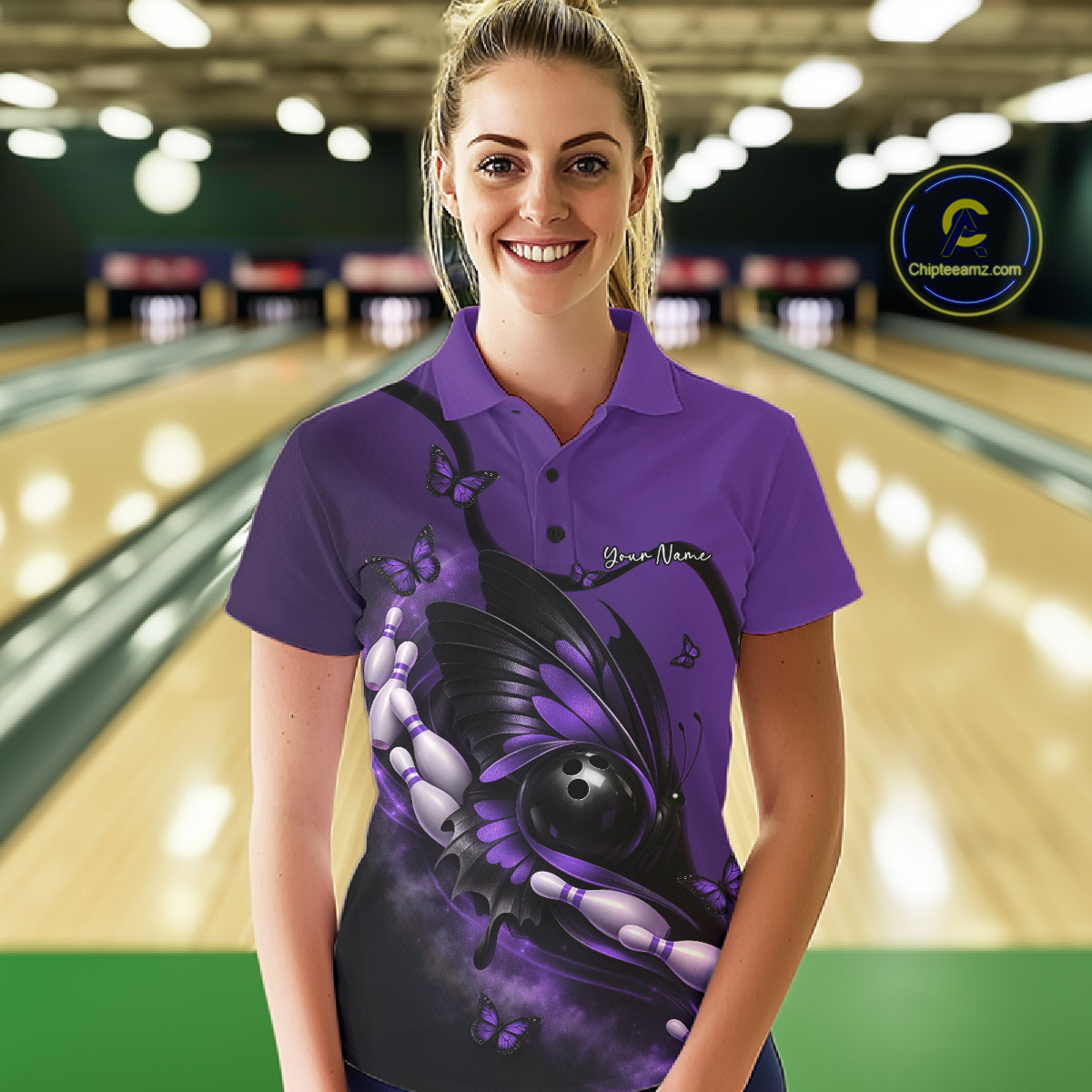 Female model wearing a purple and black bowling polo shirt at a bowling lane with butterfly artwork surrounding a bowling ball and pins.