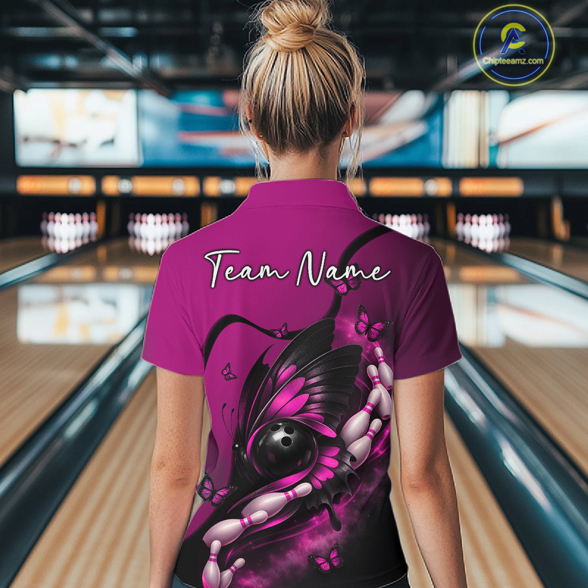Back view of a female model in a bowling alley wearing a pink and black quarter-zip shirt featuring a butterfly, bowling ball, and pin motif.