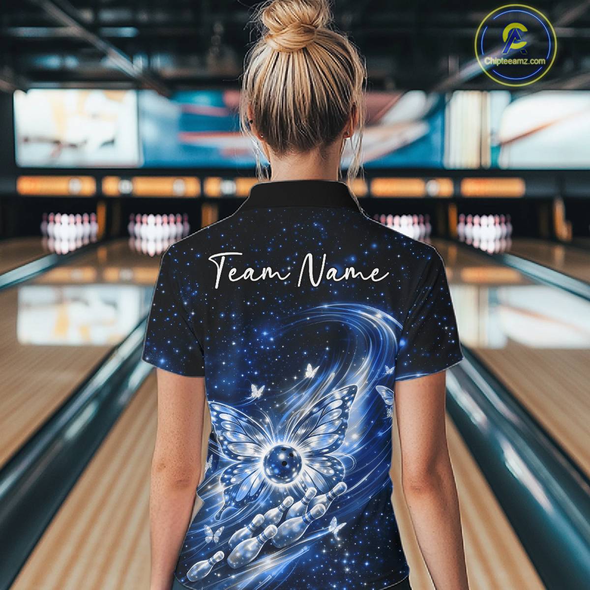 Back view of a female model wearing a blue bowling quarter-zip shirt with glowing butterfly wings, a bowling ball centerpiece, and galaxy artwork.
