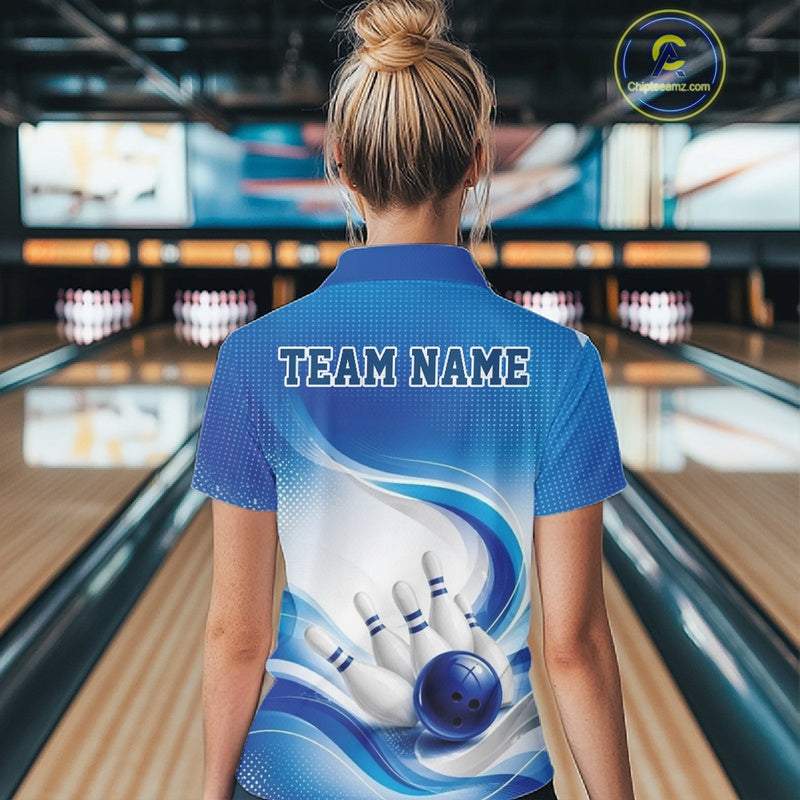 Female model standing in a bowling lane showing the back of a white and blue bowling quarter-zip shirt with abstract wave lines and a glossy bowling ball striking pins graphic.
