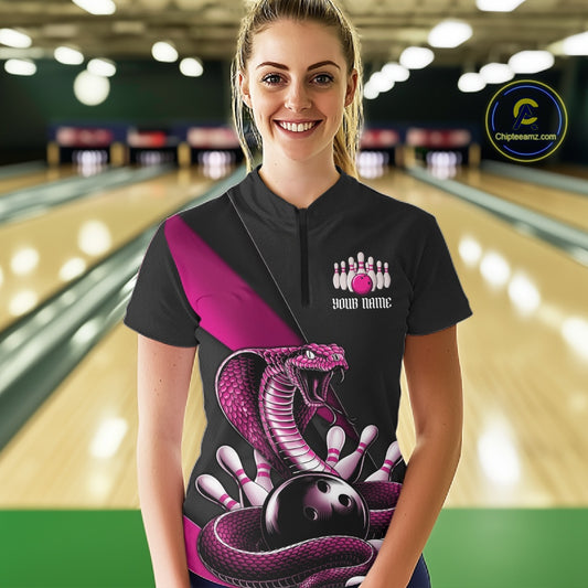 Female model wearing a black bowling quarter-zip at a bowling alley with pink cobra artwork surrounding a bowling ball.
