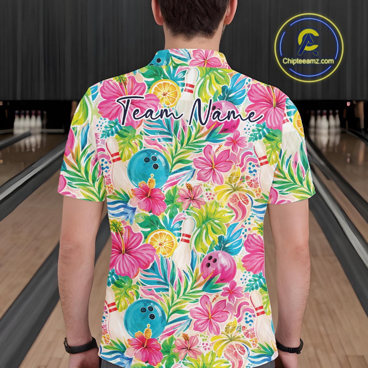 A man viewed from behind wearing a short-sleeve polo shirt with a colorful tropical bowling-themed print. The shirt features pink hibiscus flowers, green palm leaves, blue bowling balls, and the words 'Team Name' printed across the upper back.