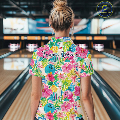 A woman viewed from behind in a bowling alley, wearing a short-sleeve collared polo shirt with a colorful tropical floral print featuring pink hibiscus flowers, green leaves, blue bowling balls, and orange citrus slices. The shirt has a custom name printed across the upper back reading 'Team Name'.