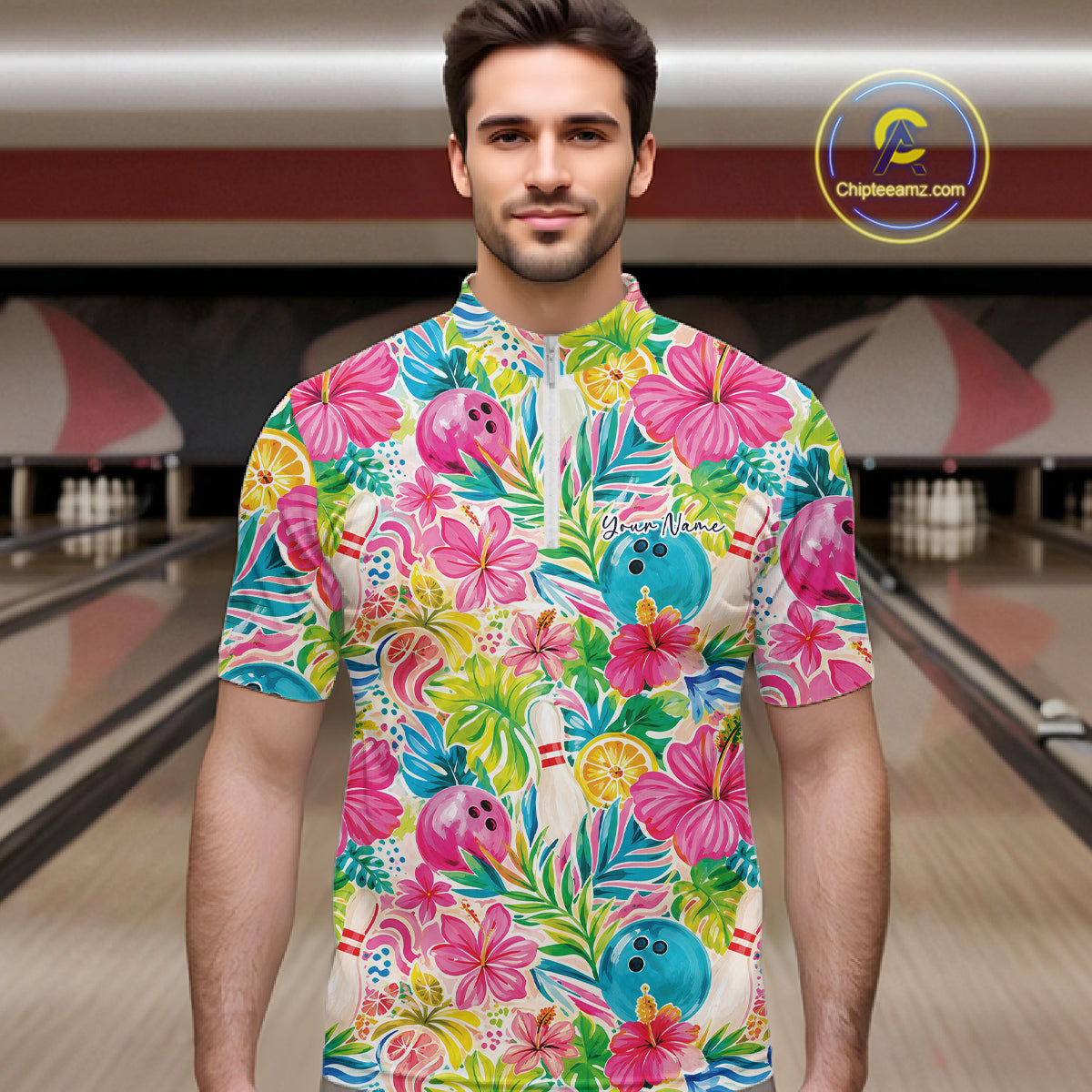A man wearing a colorful tropical floral bowling-themed short-sleeve quarter zip shirt, standing in front of a blurred bowling alley background. The shirt features pink hibiscus flowers, blue bowling balls, and green palm leaves