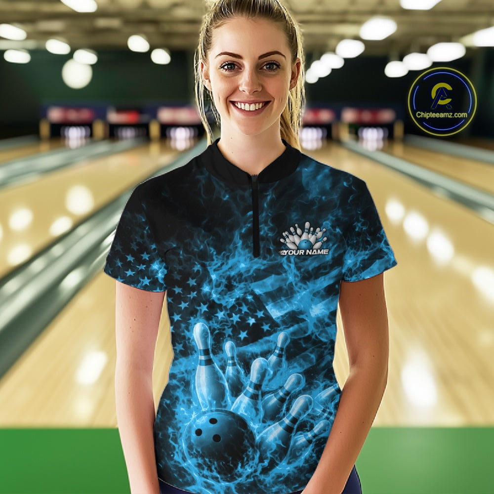Female model wearing a black and blue bowling quarter-zip in a bowling center with fiery bowling-themed artwork and flag-inspired graphics.