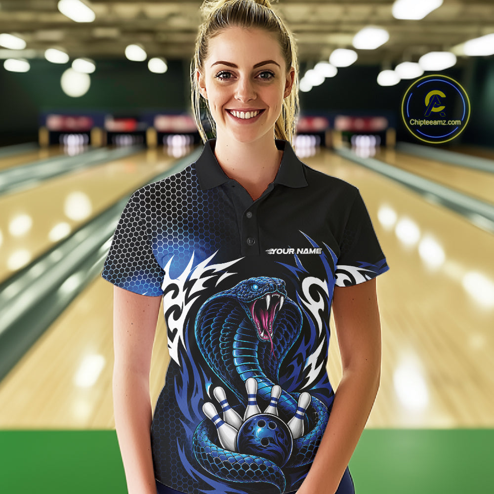 A woman stands in a bowling alley wearing a black short-sleeve polo shirt with a large blue snake graphic, bowling pins, and white tribal-style patterns. 
