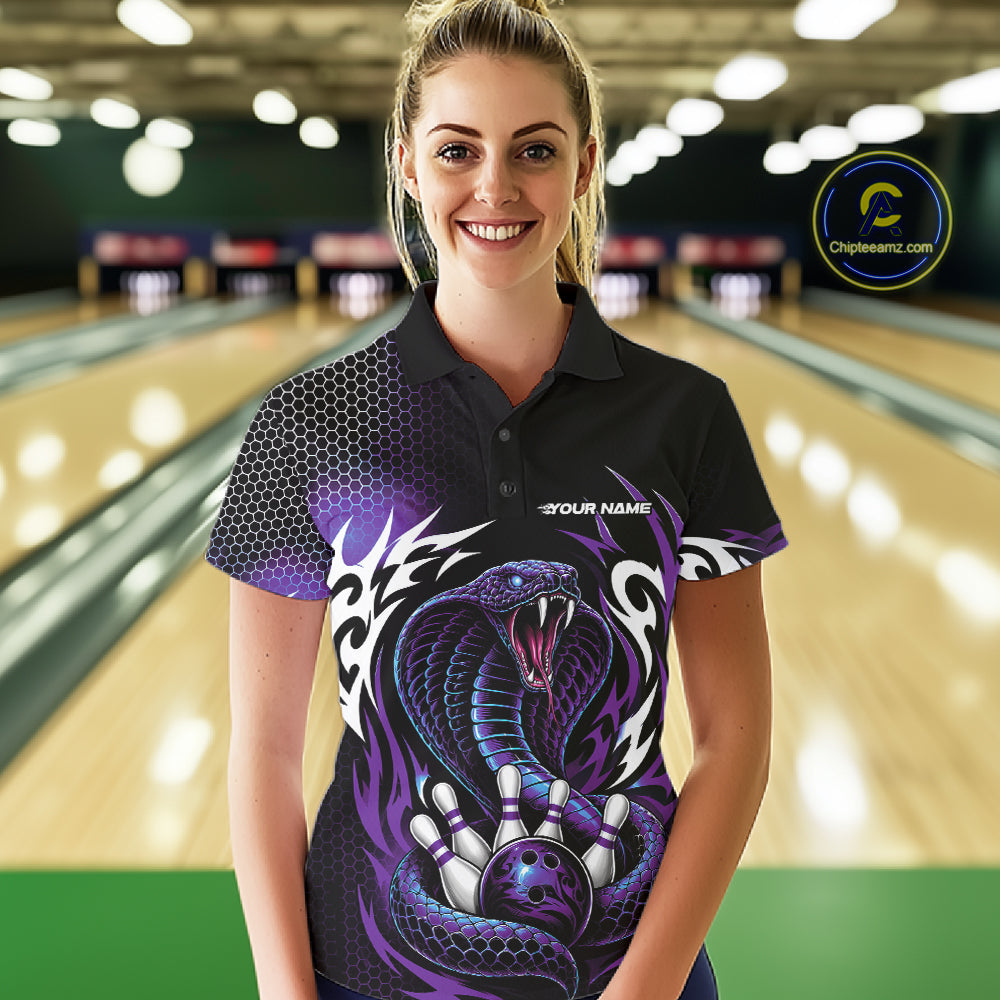 A woman stands in a bowling alley wearing a black short-sleeve polo shirt with a large purple cobra snake graphic on the front, along with bowling-themed text and a bowling pin graphic. 