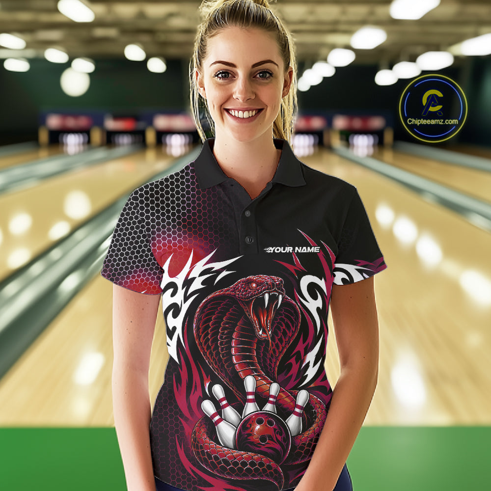 A woman wearing a black short-sleeve bowling polo shirt with a red and white cobra snake graphic, standing in a bowling alley. The shirt features a red and black cobra snake design with white tribal-style accents, and the text 'YOUR NAME' on the chest.