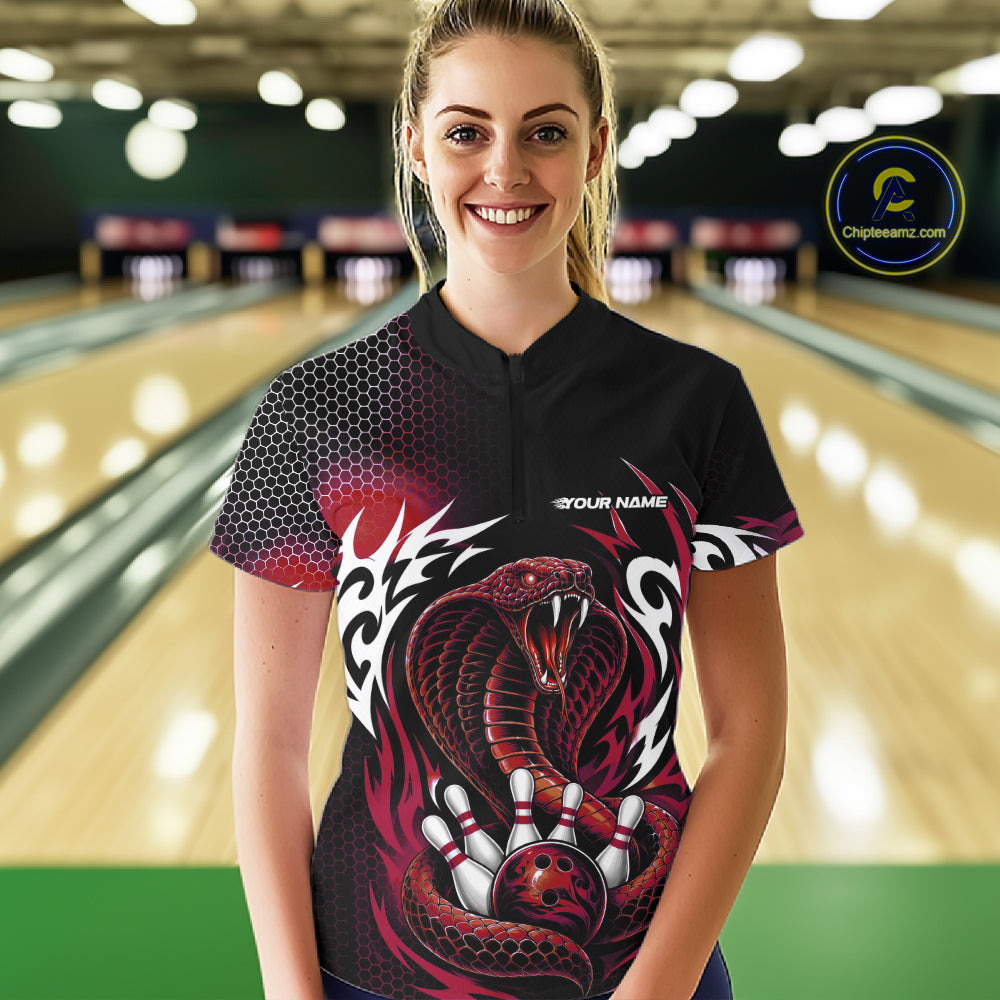 A woman wearing a black bowling-themed short-sleeve quarter zip shirt with a red and white snake graphic, standing in a bowling alley. 
