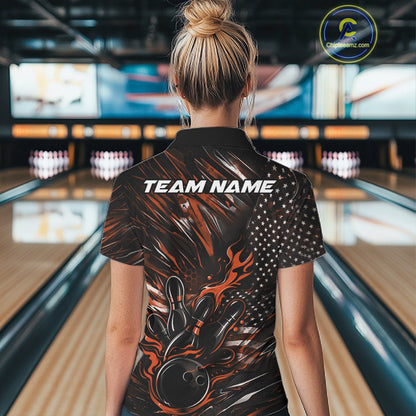 Back view of a female model in a bowling alley wearing a black and orange polo shirt featuring a flaming bowling ball and patriotic bowling motif.