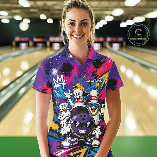 A woman stands in a bowling alley wearing a colorful custom bowling-themed polo shirt with cartoon bowling characters and a purple bowling ball graphic. The background shows blurred bowling lanes.