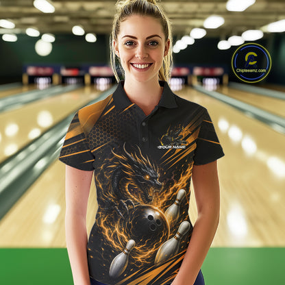 A woman wearing a black short-sleeve polo shirt with a detailed graphic print of a dragon, bowling ball, and bowling pins, standing in front of a blurred bowling alley background