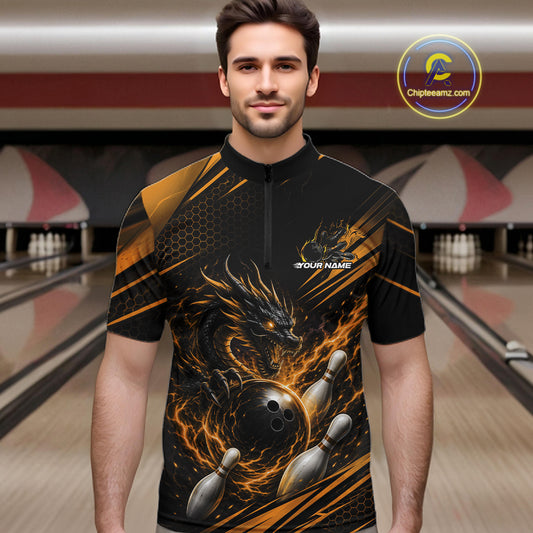A man wearing a black short-sleeve quarter-zip bowling jersey with a fiery dragon and bowling pins graphic, standing in a bowling alley. The jersey features orange and gold flame accents, a honeycomb pattern on the upper chest.