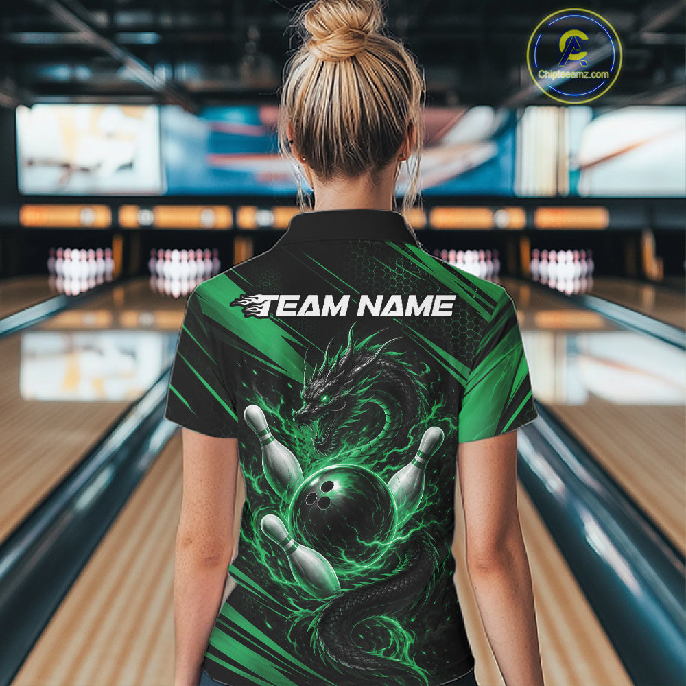 A woman viewed from behind wearing a black and green short-sleeve bowling-themed polo shirt with a dragon and bowling ball graphic, standing in a bowling alley. The shirt has 'TEAM NAME' printed across the upper back