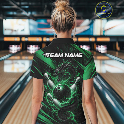 A woman viewed from behind wearing a black and green short-sleeve bowling-themed polo shirt with a dragon and bowling ball graphic, standing in a bowling alley. The shirt has 'TEAM NAME' printed across the upper back